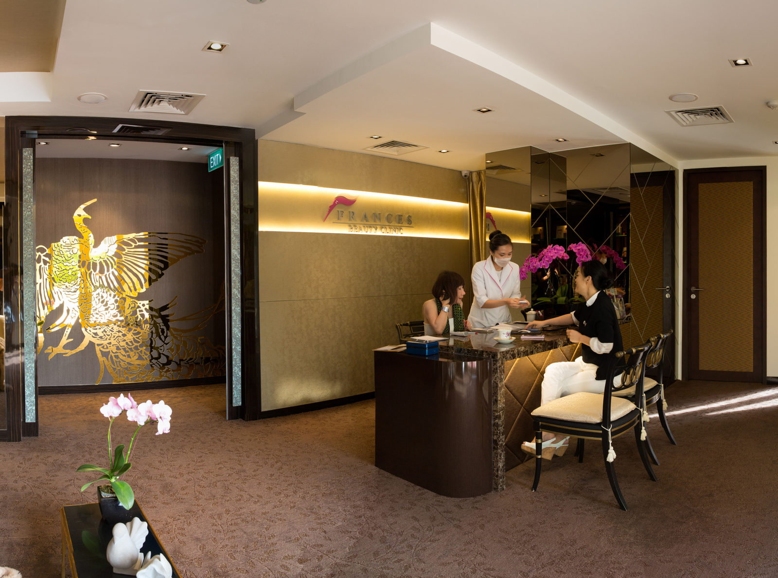 The Frances Beauty Clinic reception — a therapist attending to clients beneath the gold phoenix mural
